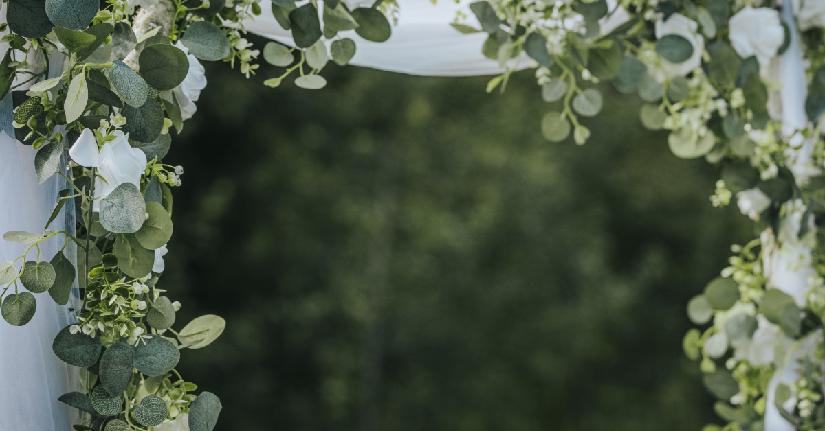 Sheer voile drape in an outdoor event fabric display. Green floral decorations hang across the fabric.